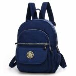 Mini sac à dos pour femme étanche de couleur unie bleu marine. Le sac à dos a quatre poches de tailles différentes. Une avec un velcro et 3 avec des zips. Sur la poche avec le velcro, il y a le logo du sac. Le sac a une hanse pour le tenir sur un crochet et deux hanses pour pouvoir le porter sur le dos.