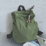 Sac à dos de voyage en toile vert avec un mur gris