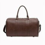 Grand sac de voyage imperméable en imitation cuir en version marron, sur fond gris clair.