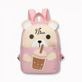 Petit sac à dos rose pour enfant en forme de nounours sirotant un verre avec une paille où il est inscrit le prénom Nina, sur fond gris clair