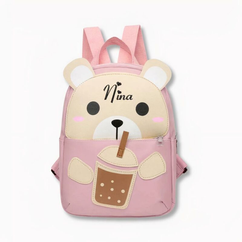 Petit sac à dos rose pour enfant en forme de nounours sirotant un verre avec une paille où il est inscrit le prénom Nina, sur fond gris clair