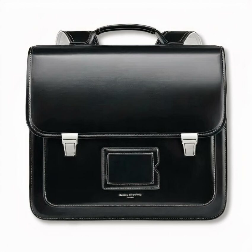 Cartable noir d'écolier traditionnel avec un porte carte devant, sur fond gris clair