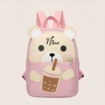 Petit sac à dos rose pour enfant en forme de nounours sirotant un verre avec une paille où il est inscrit le prénom Nina, sur fond mauve.