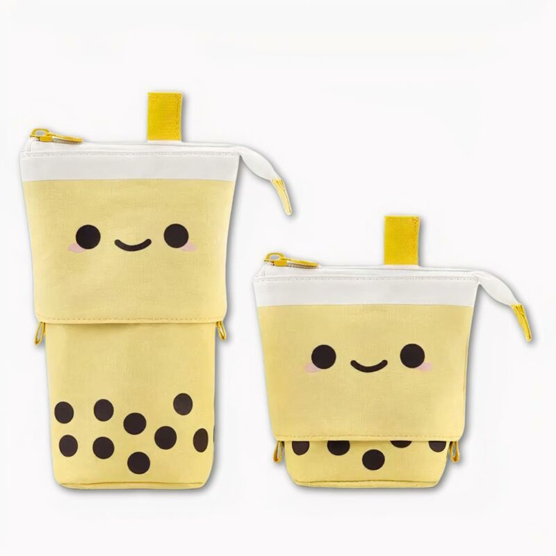 Photo d'une trousse en forme de Bubble Tea, de couleur jaune avec un petit visage et des bulles noir en bas. Il y a également une petite languette en haut en guise de paille, une fermeture éclair. La trousse s'ouvre en rétractant la partie haute. Le fond de l'image est gris clair.