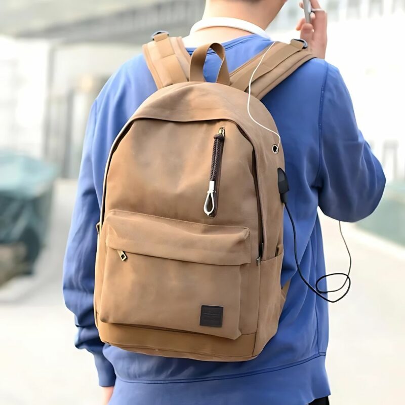 Jeune homme portant le grand sac à dos chargeur USB sur son dos. IL est en train d etéléphoner tandis que son téléphoen se recharge tout seul sur la prise USB de son sac.