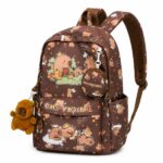 Un sac à dos capybara illustrant une scène de prairie marron, avec de petits dessins de capybaras, une poche ronde et une peluche accrochée sur le côté.